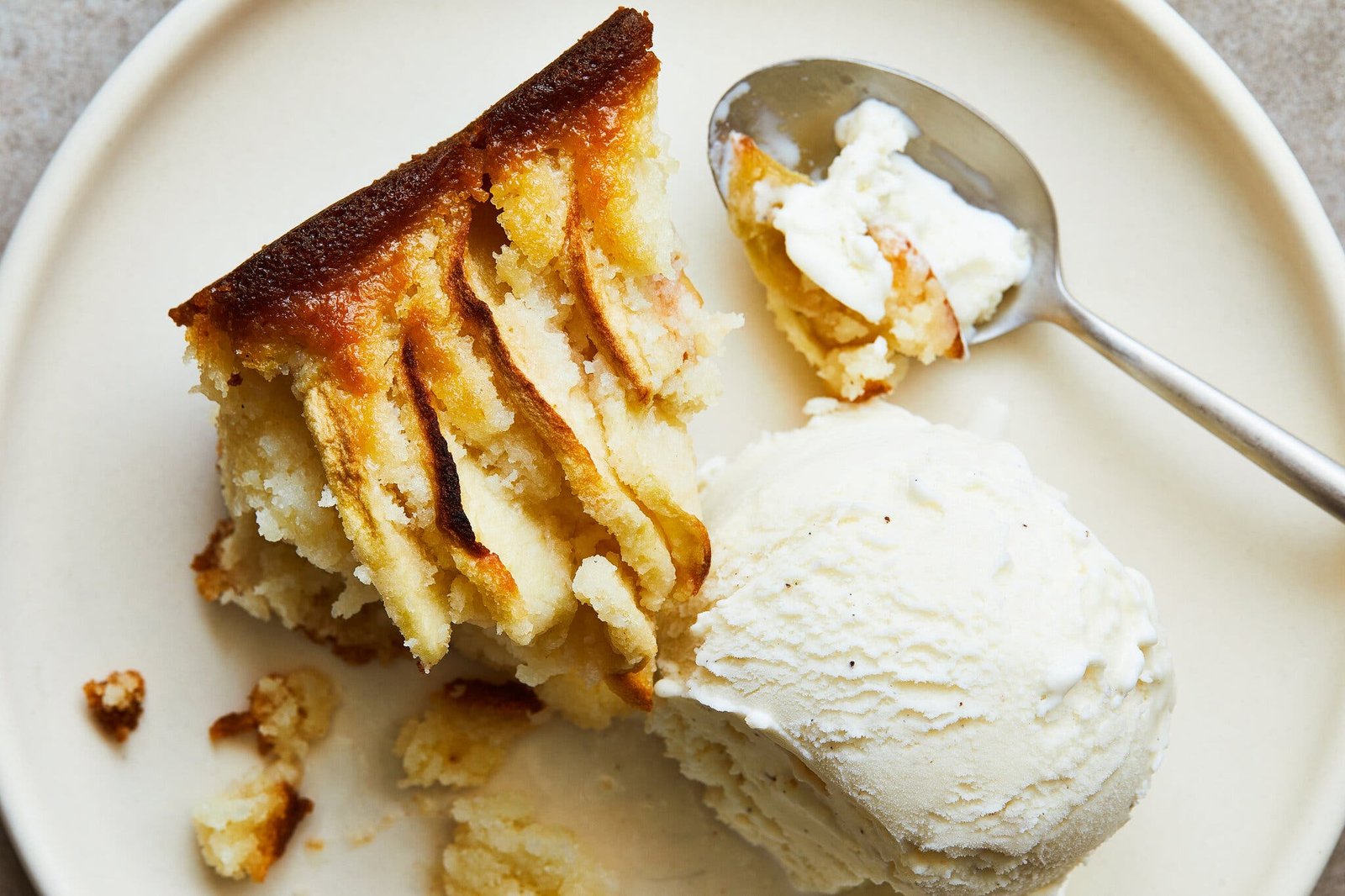 A white plate with a slice of apple buckle and a scoop of vanilla ice cream.