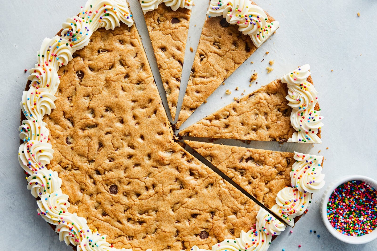 A chocolate chip cookie cake decorated with vanilla buttercream and rainbow sprinkles.