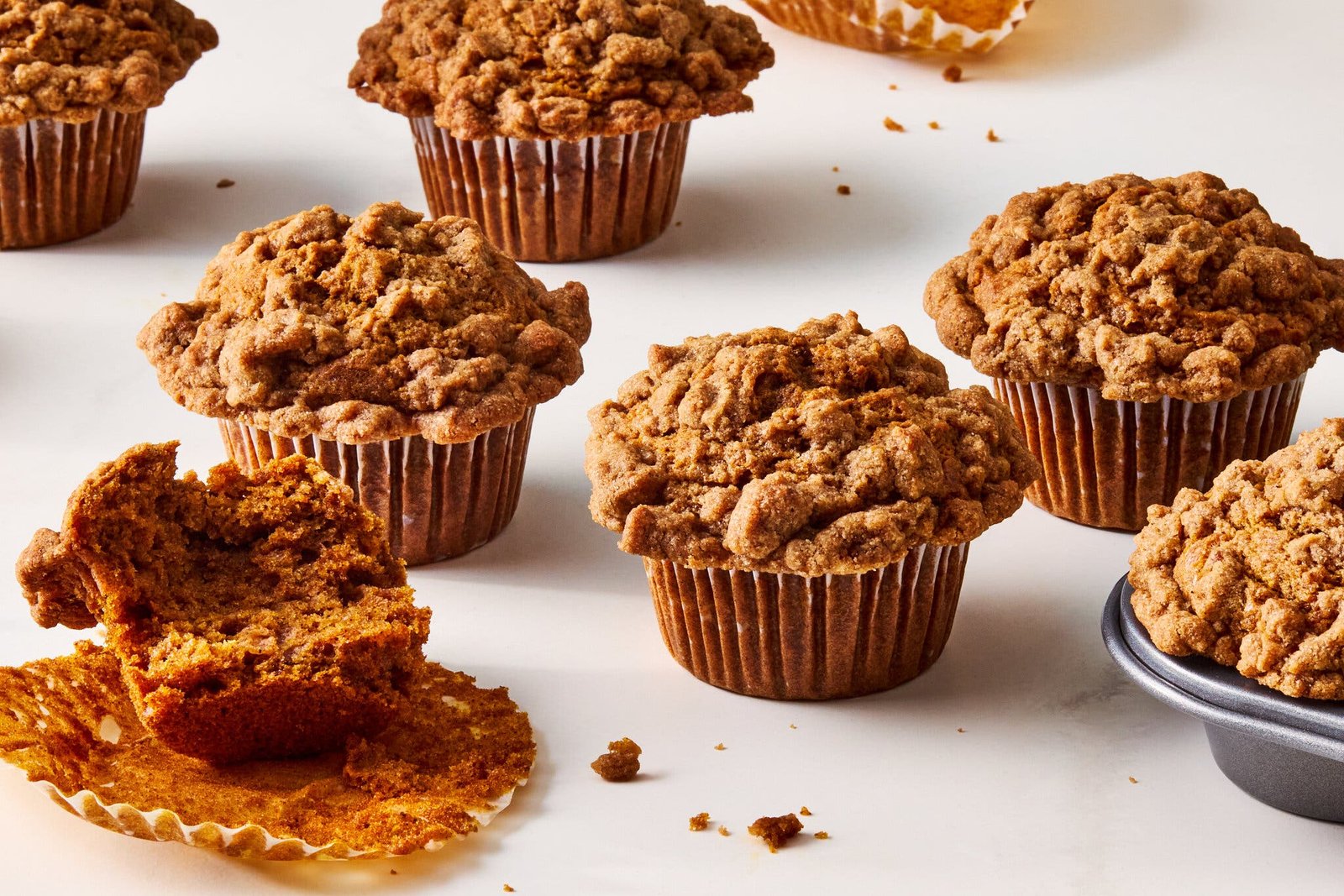 Pumpkin cardamom crumb muffins on a counter top. One of them is half eaten.