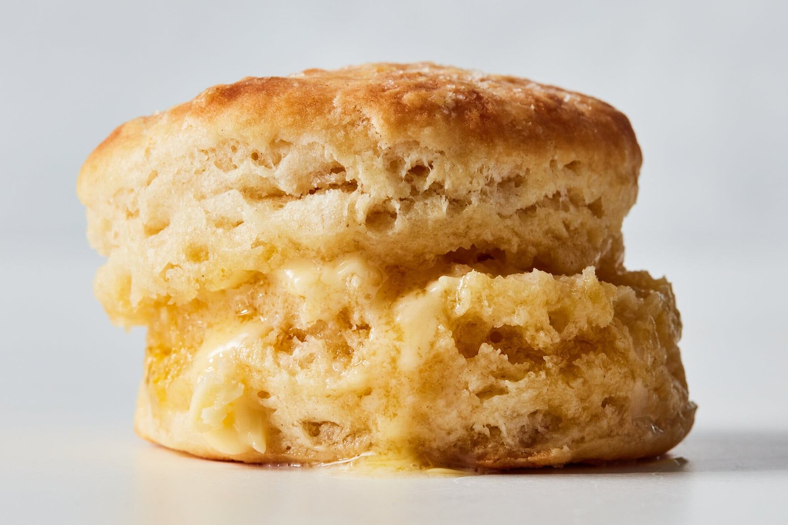 A fluffy, golden biscuit has been split, filled with melted butter and restacked.