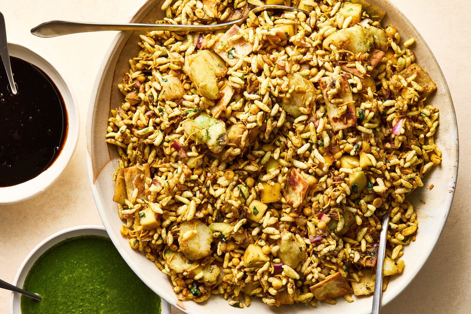 A large dish is filled with bhel puri and two sauces are in bowls next to it.