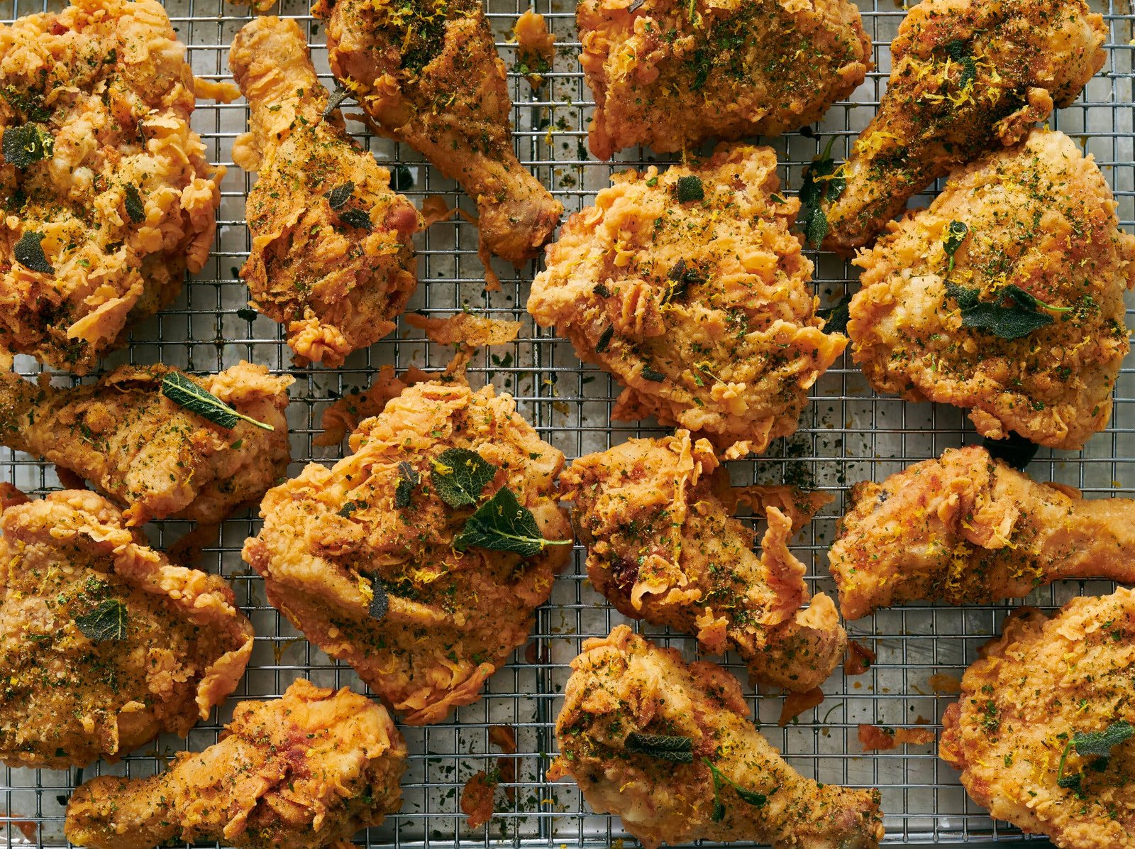 Craggy pieces of fried chicken topped with sage sit on a baking rack.