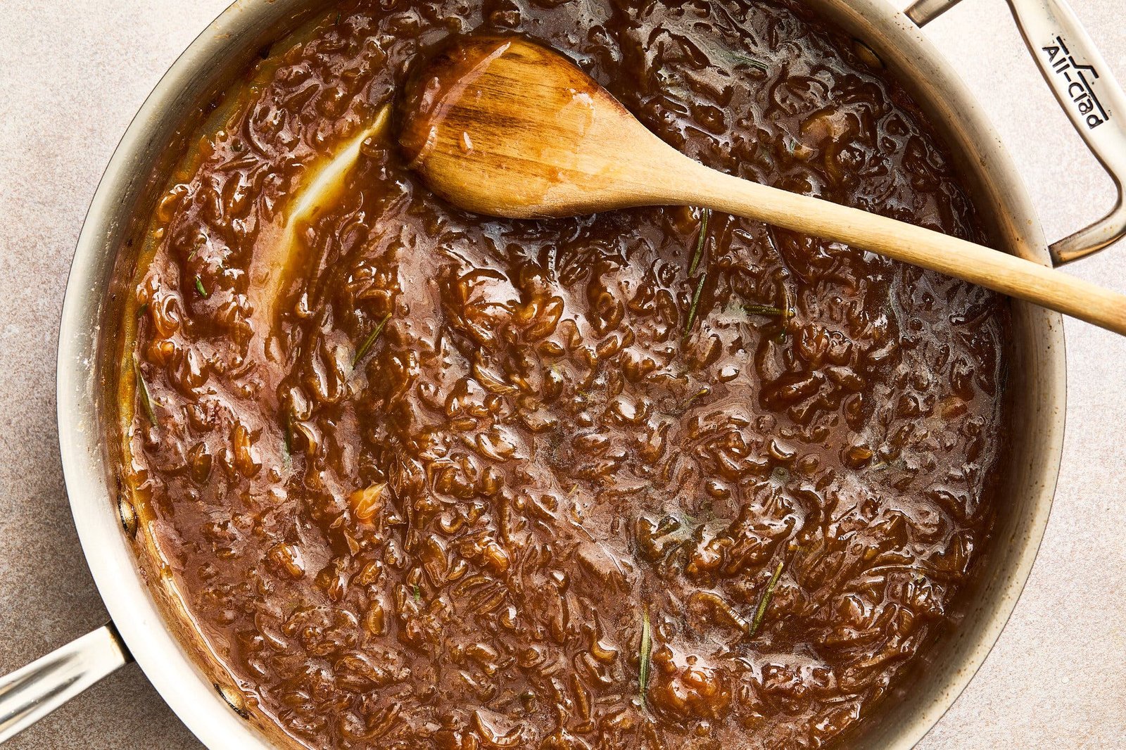 A deep skillet is filled with brown gravy and holds a wooden spoon.