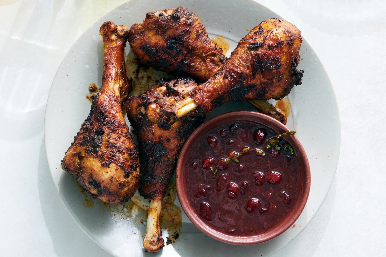 Four turkey drumsticks are on a plate with a bowl of cranberry sauce.