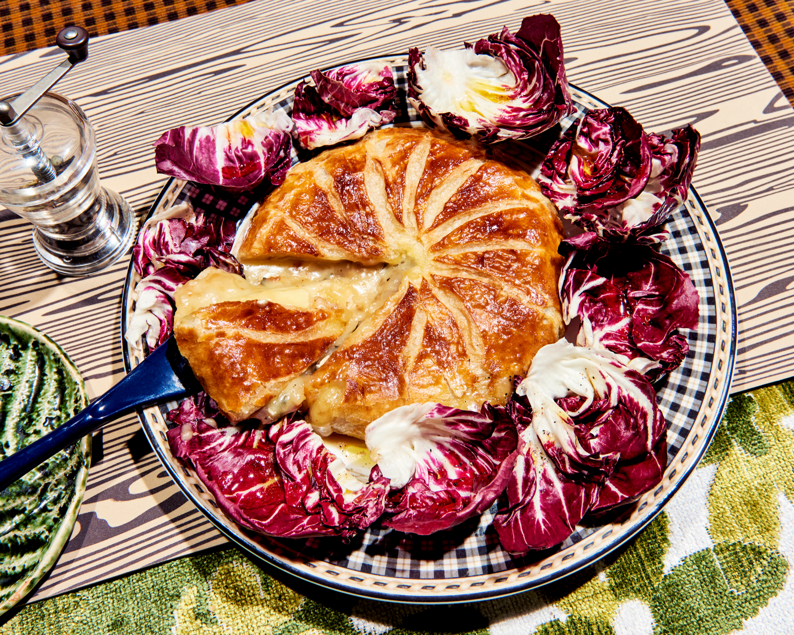 An overhead image of a plate topped with a puff pastry covered Brie surrounded by radicchio leaves.