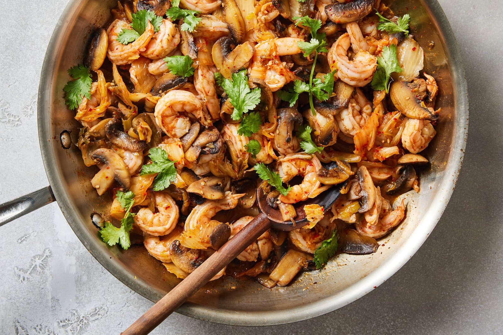 An overhead image of a skillet filled with cooked mushrooms and shrimp and topped with herbs.