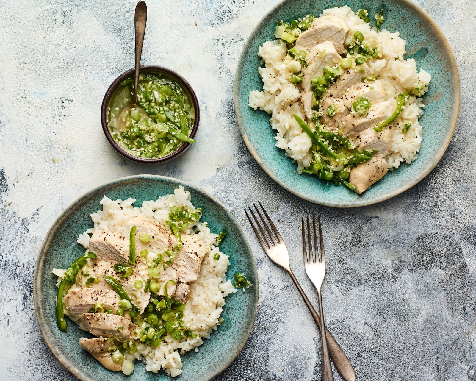 Sliced pieces of chicken on a bed of rice are finished with a green scallion ginger sauce.