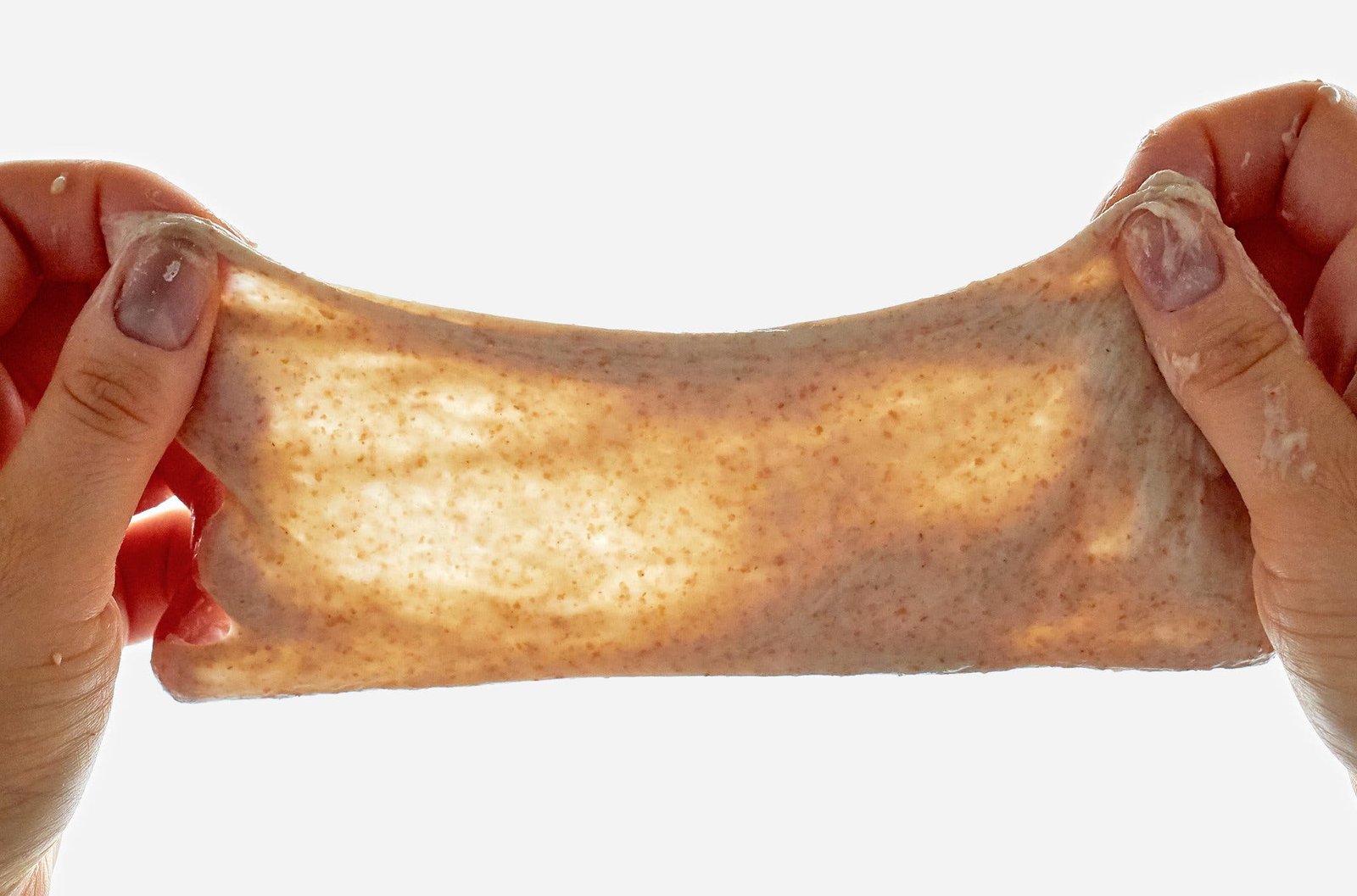 Two hands hold up a stretched piece of dough.