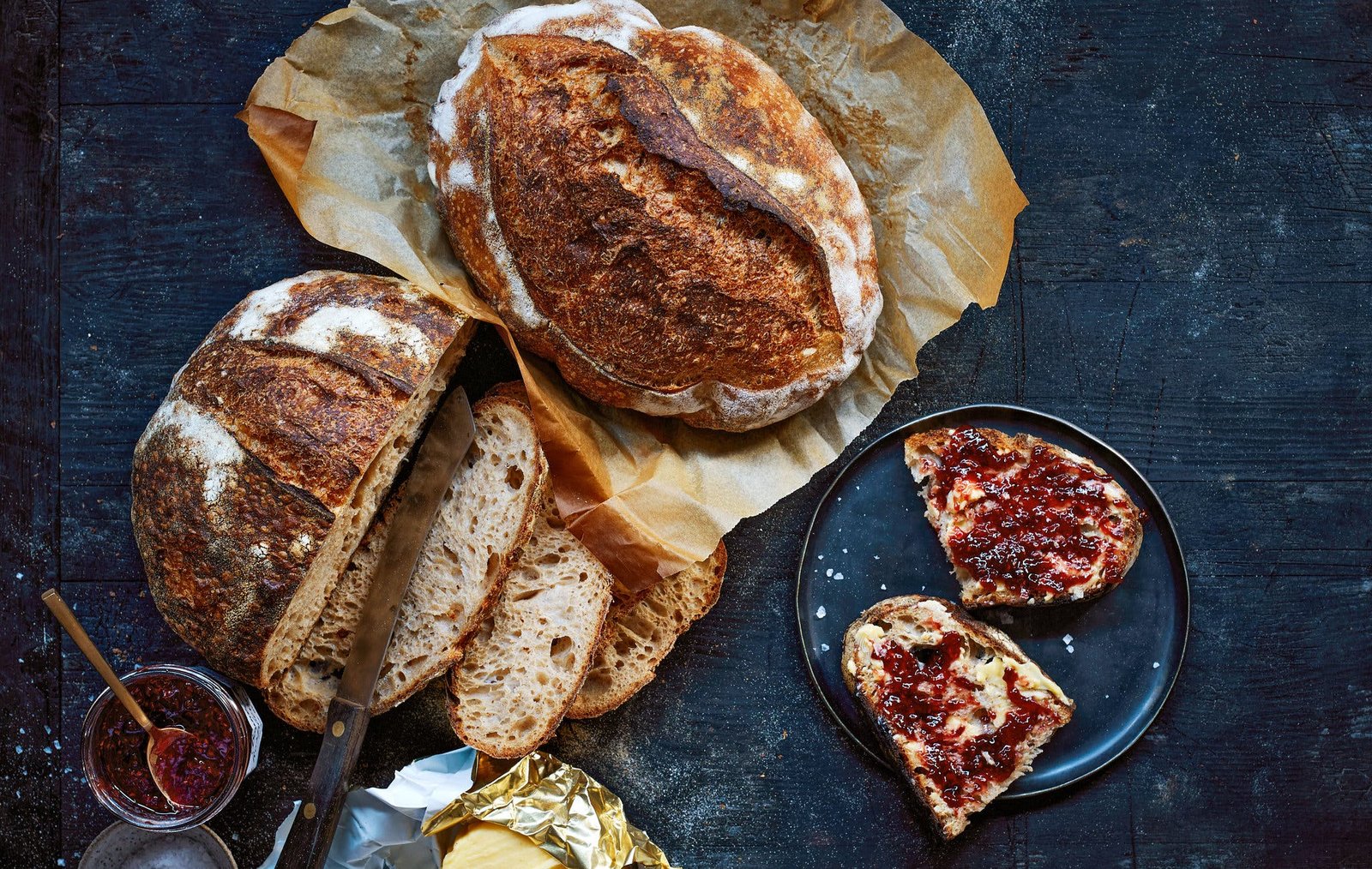 An overhead image of finished sourdough bread next to a slice of jam covered toast.