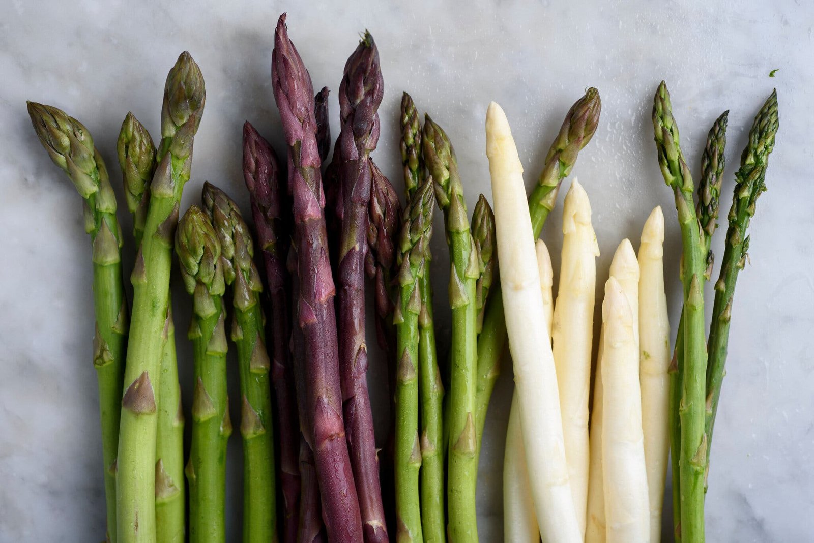 An overhead image of several kinds of asparagus on a marble surface.