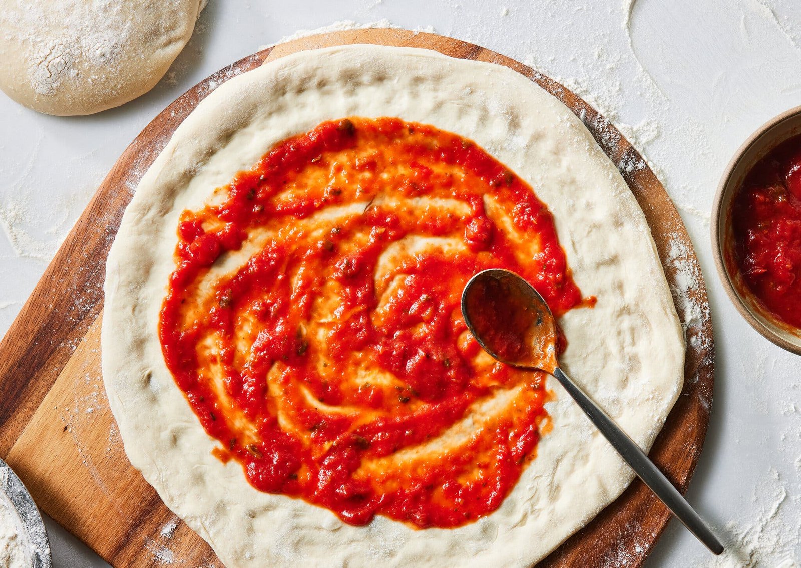 An overhead image of rolled out pizza dough topped with tomato sauce.