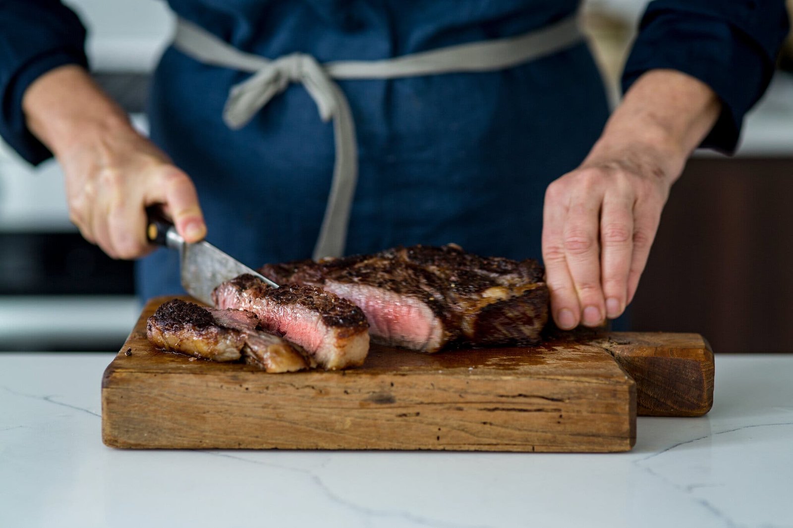 A side image of a cook slicing a thick rib-eye steak on a cutting board.