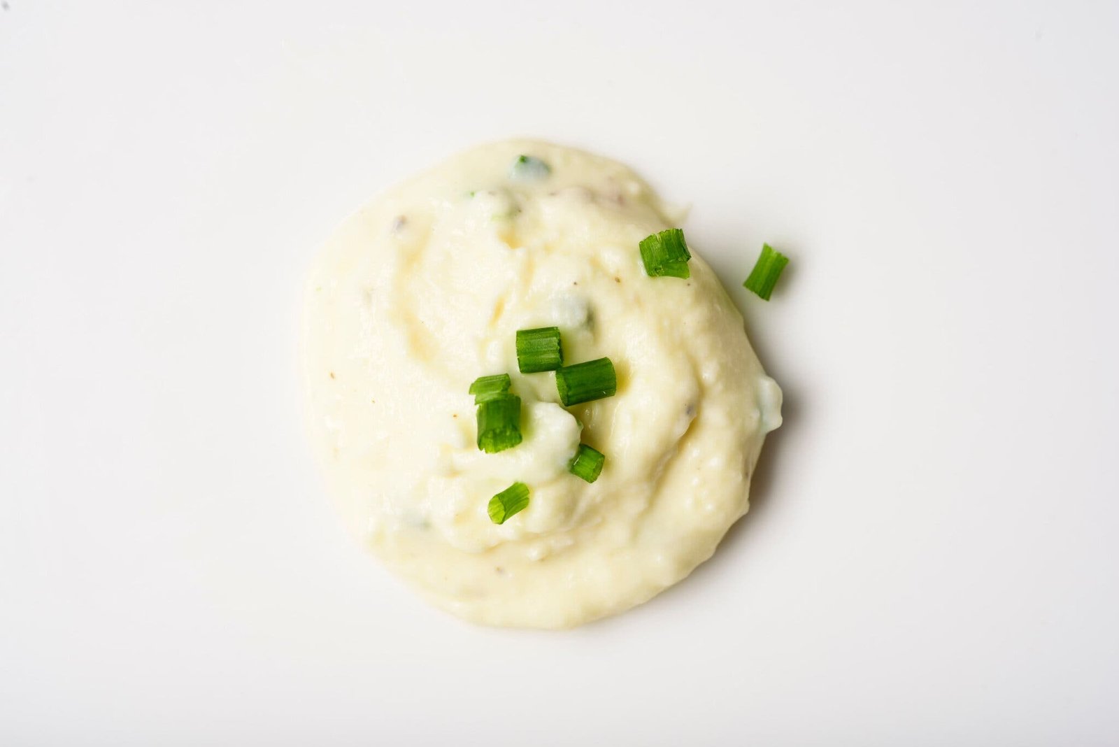 An overhead image of a white sauce with chives on top.