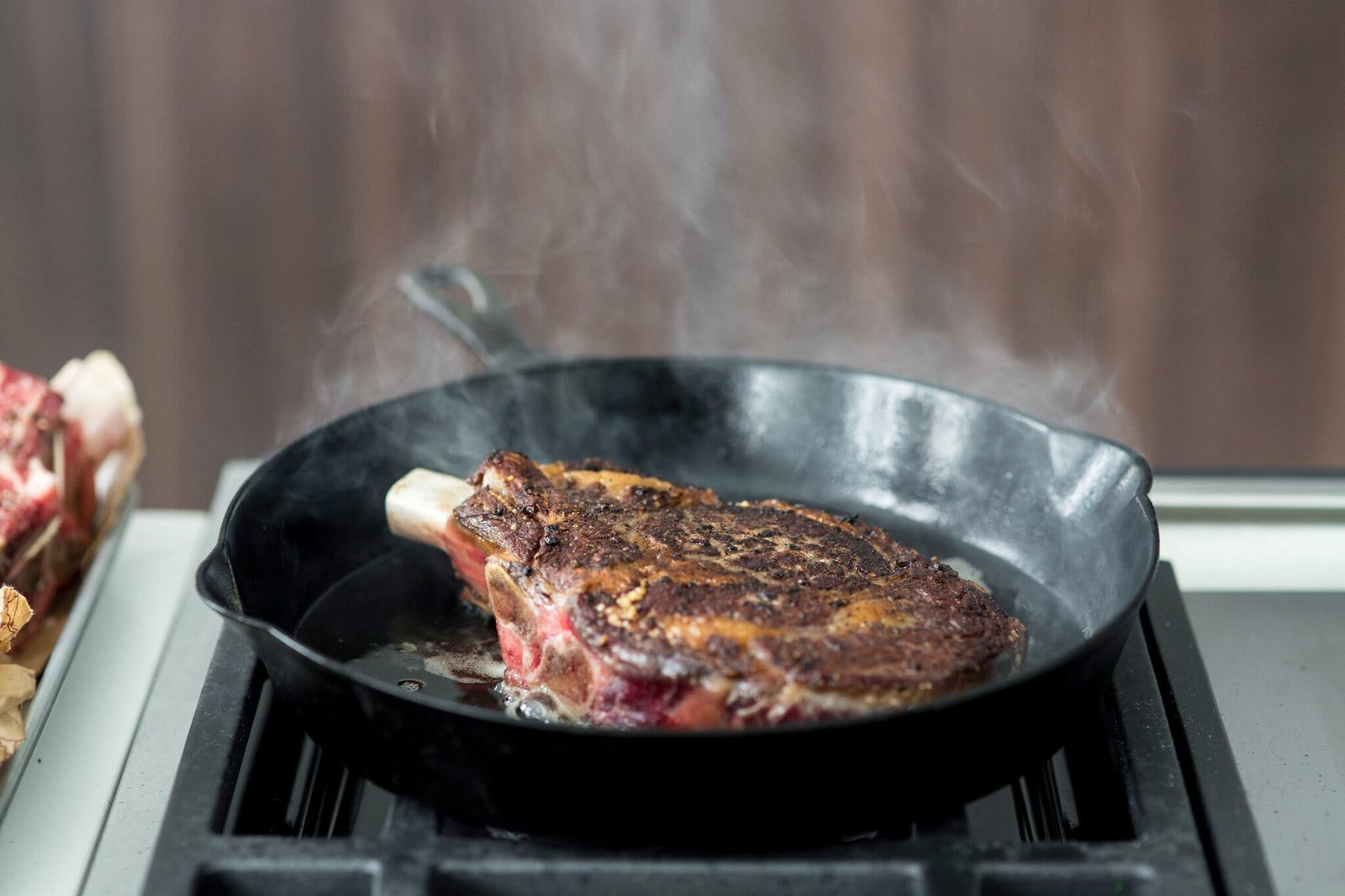 A steak sizzles on the stove in a cast-iron skillet.