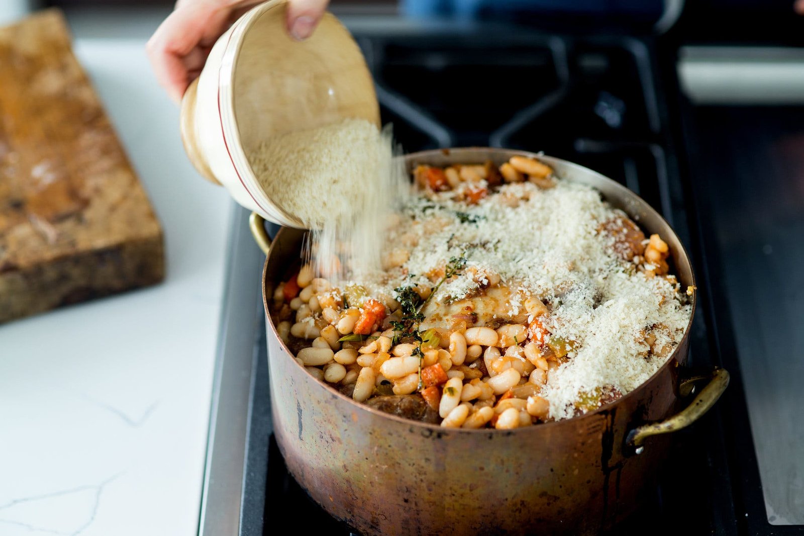 A side image of a cassoulet in a pot being topped with bread crumbs.
