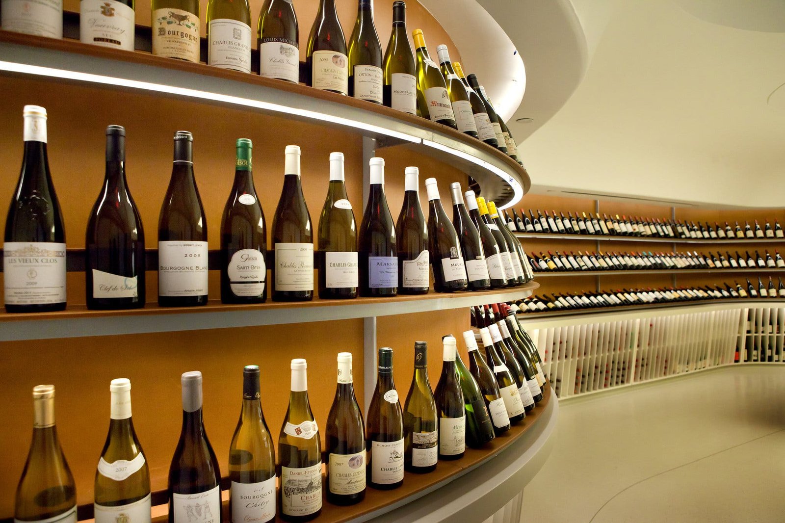Wine bottles displayed on curved shelves, varied colors and labels visible.