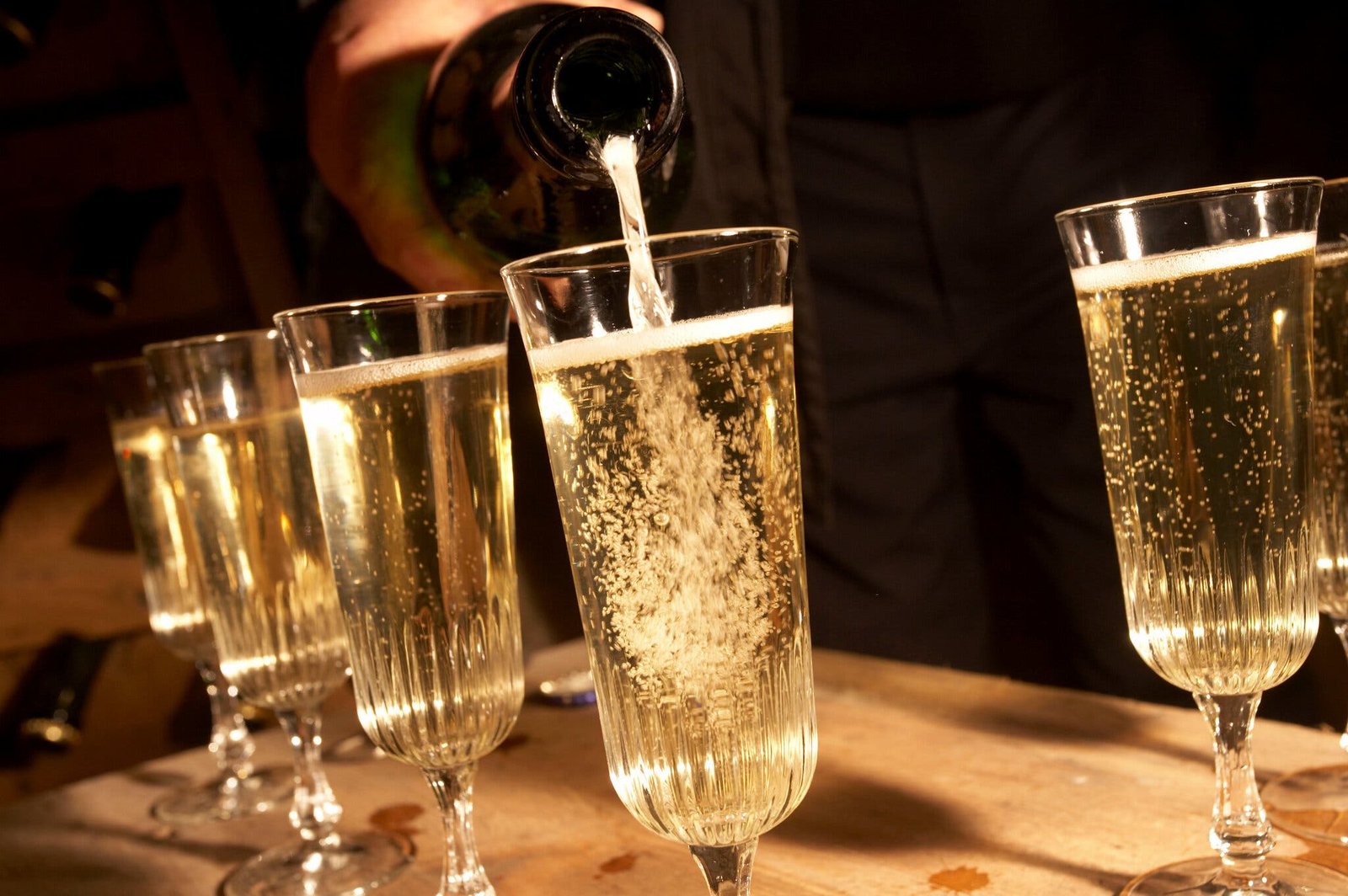 A hand holding a bottle pours sparkling wine into glasses.