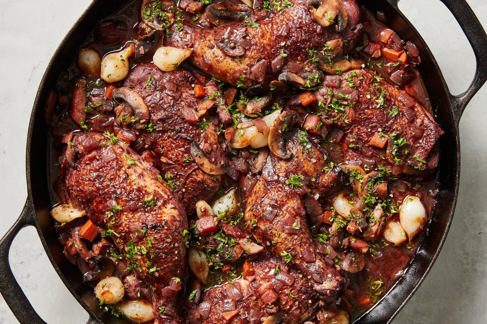 An overhead image of coq au vin in a large cast iron Dutch oven.