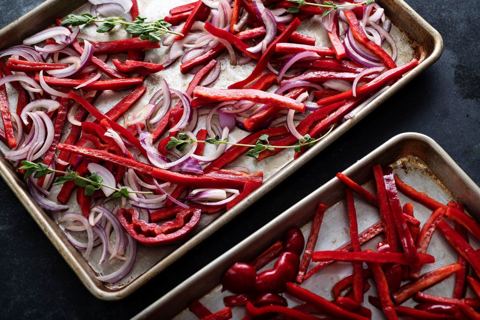 Sliced red peppers and red onions sit on sheet pans.