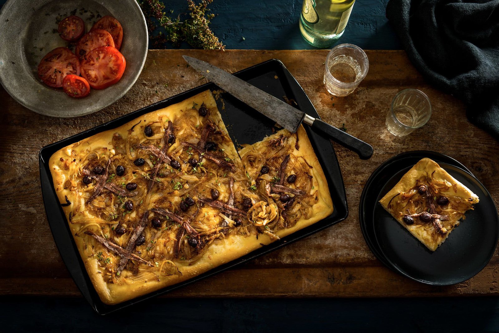 A small sheet pan filled with a pizzalike flatbread topped with onions, garlic, thyme and anchovies.