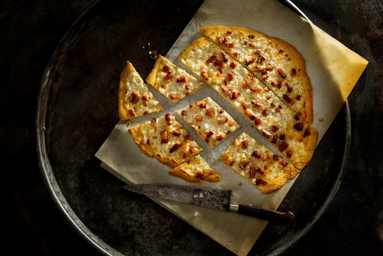 An overhead image of a pizzalike dough topped with caramelized onions, bacon and fromage blanc.