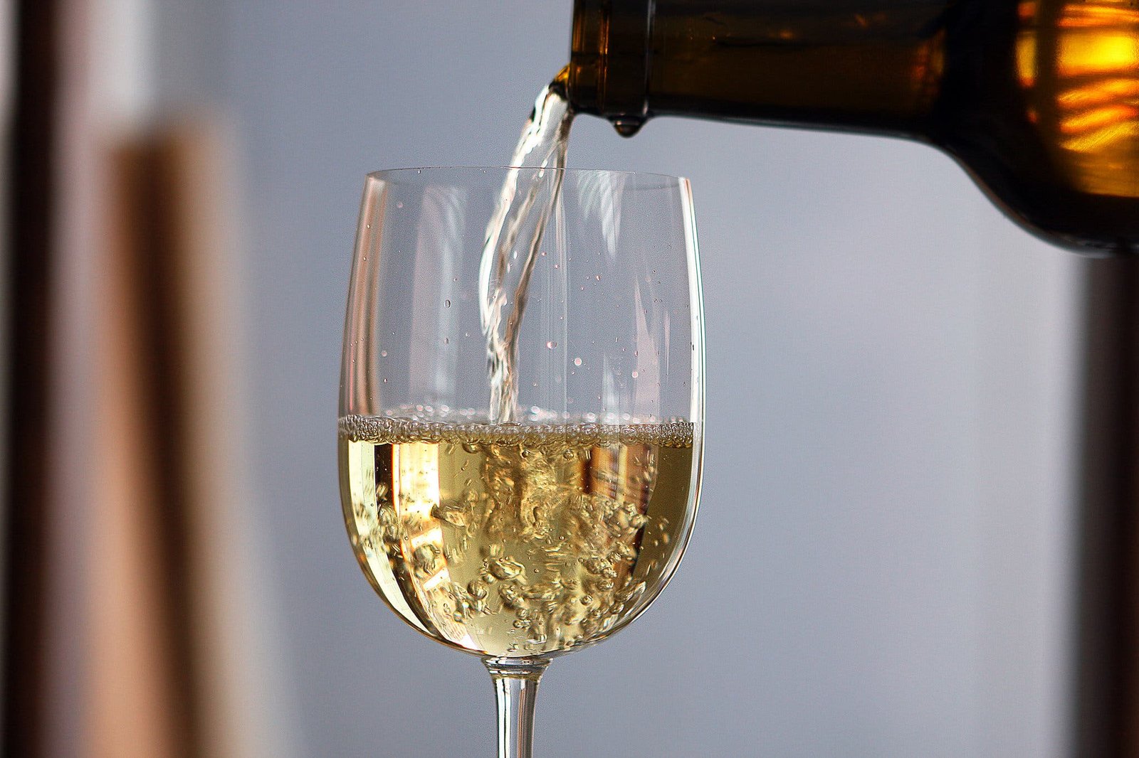 A side image of a stemmed glass being filled with white wine.