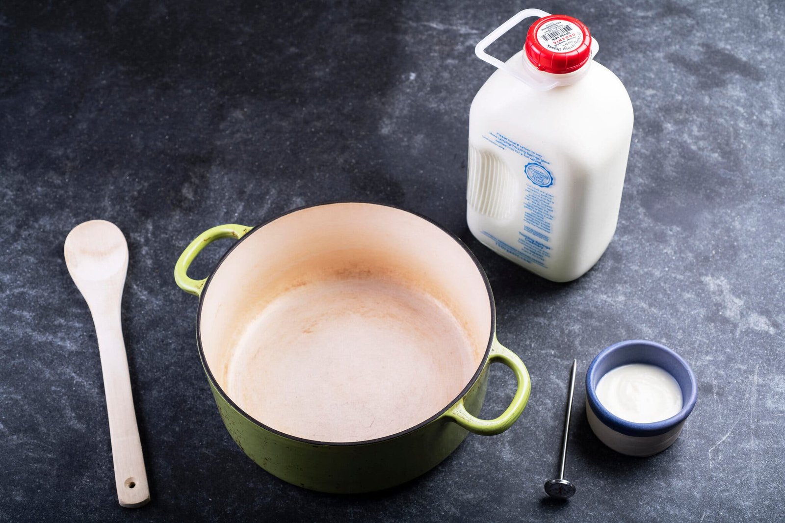 An overhead image of the equipment and ingredients needed for yogurt, including a Dutch oven, milk and starter.