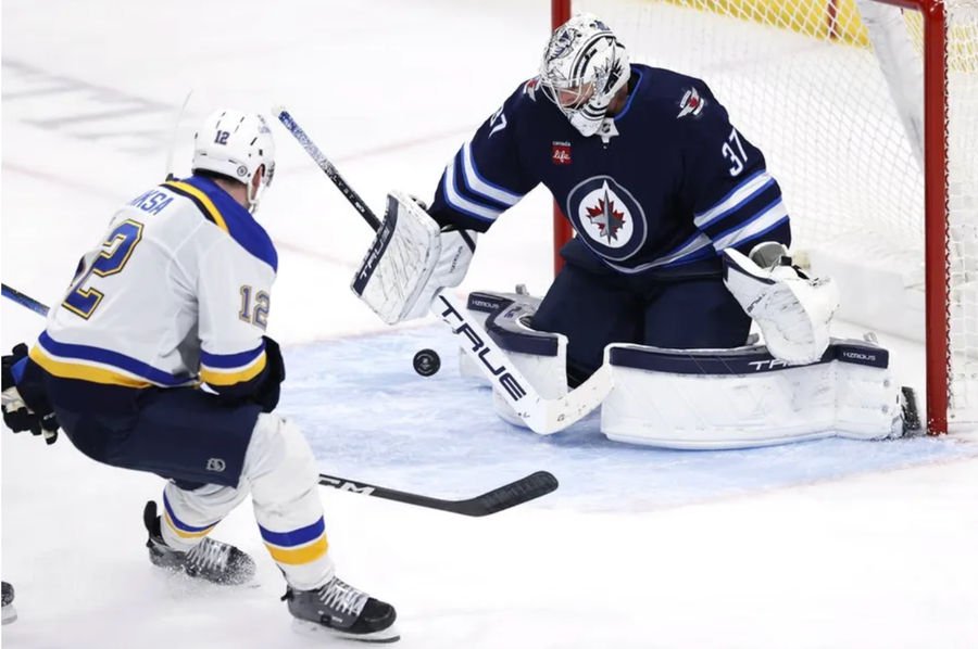 Apr 7, 2025; Winnipeg, Manitoba, CAN; Winnipeg Jets goaltender Connor Hellebuyck (37) blocks a shot from St. Louis Blues center Radek Faksa (12) in the third period at Canada Life Centre. Mandatory Credit: James Carey Lauder-Imagn Images