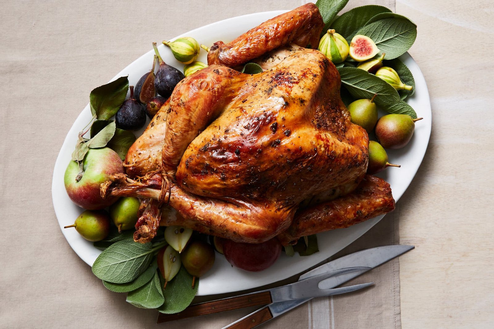 An overhead image of a burnished roast turkey surrounded by herbs, apples, pears and figs.