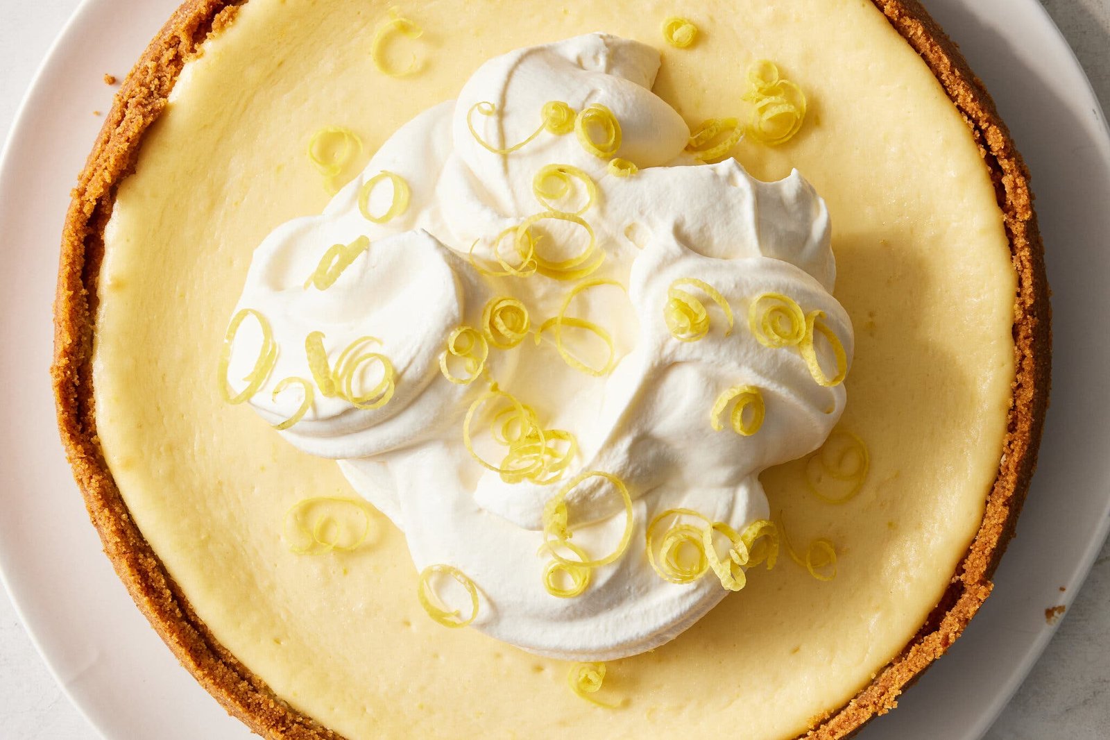 An overhead image of a yellow lemon cheesecake topped with whipped cream and lemon zest.