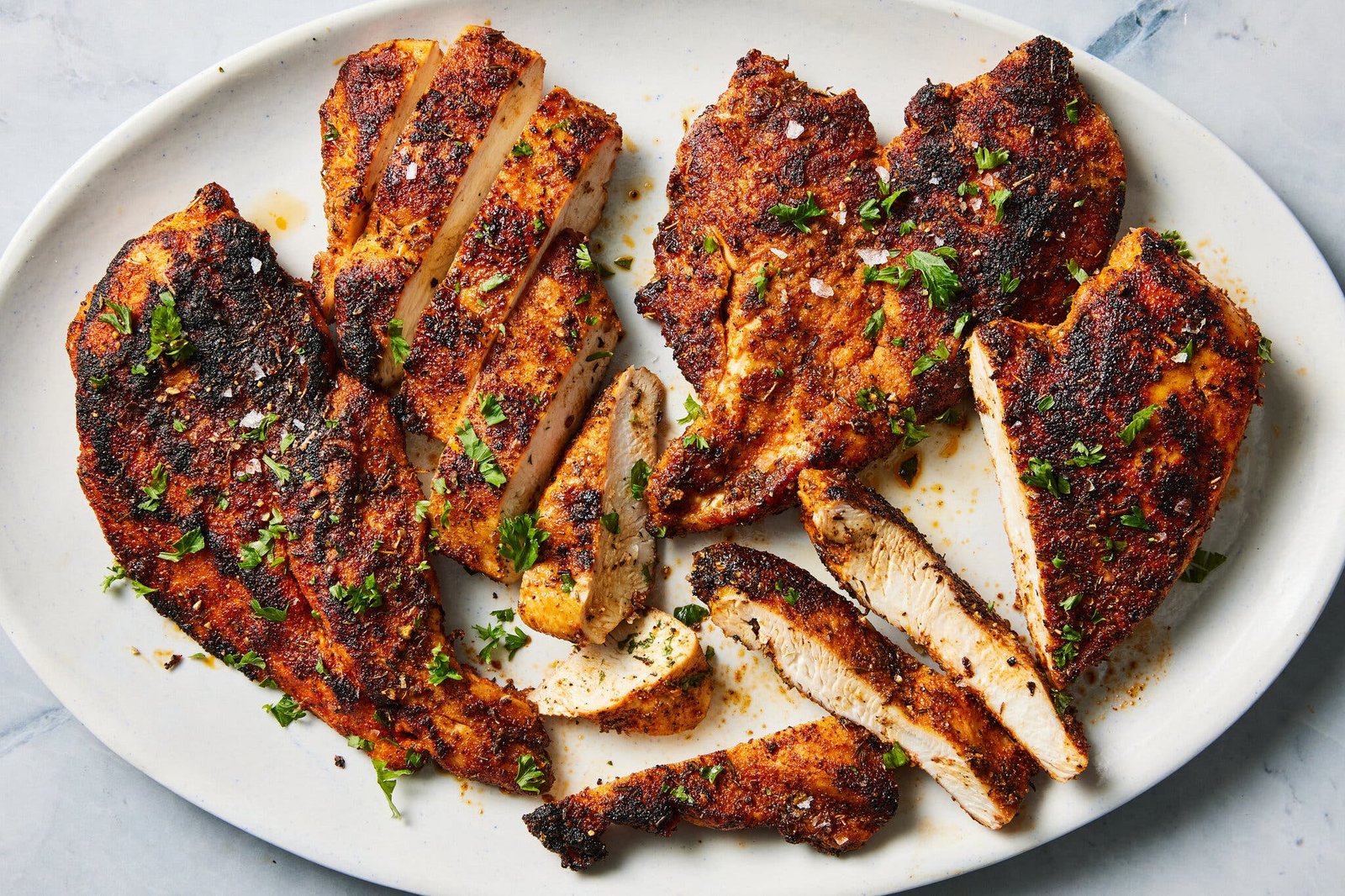 An overhead image of chicken breasts coated in a dark spice rub on a white platter.