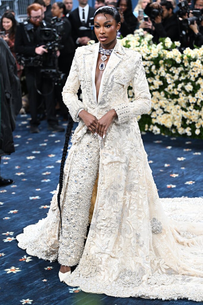 Coco Jones is wearing a jeweled white suit with a long train.